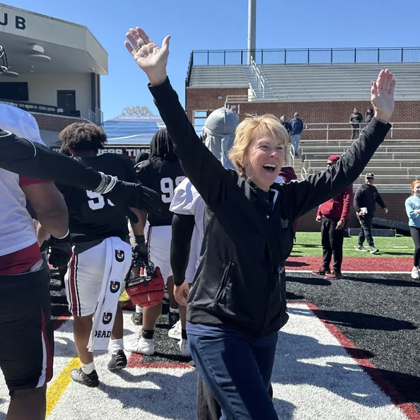 A DFC volunteer with both arms in the air, cheering beside the football team on the field