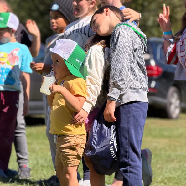 Campers lined up on the grass watching the games, the youngest in a green Dexcom cap holding a drink