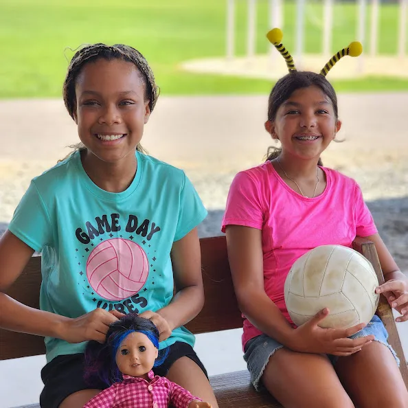 Two campers sitting together on a bench with a volleyball on game day