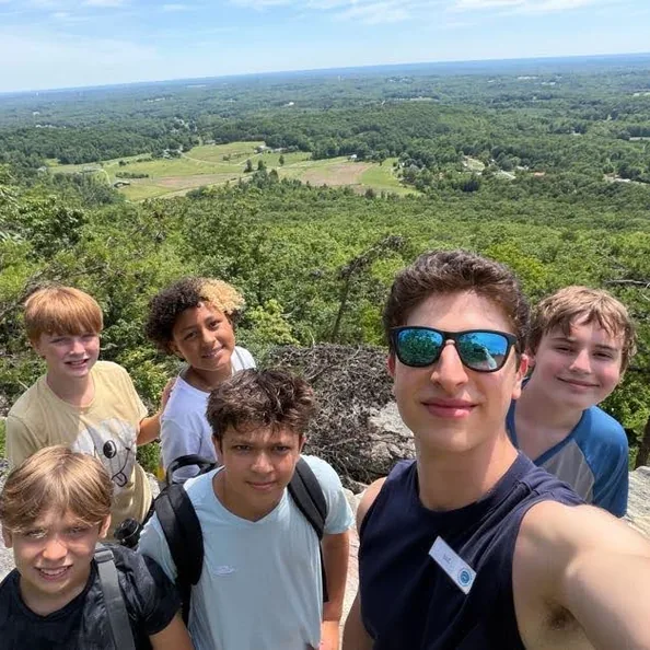 Five Camp Morris campers and a counselor crowded into a selfie at a rocky overlook, green Piedmont farmland far below