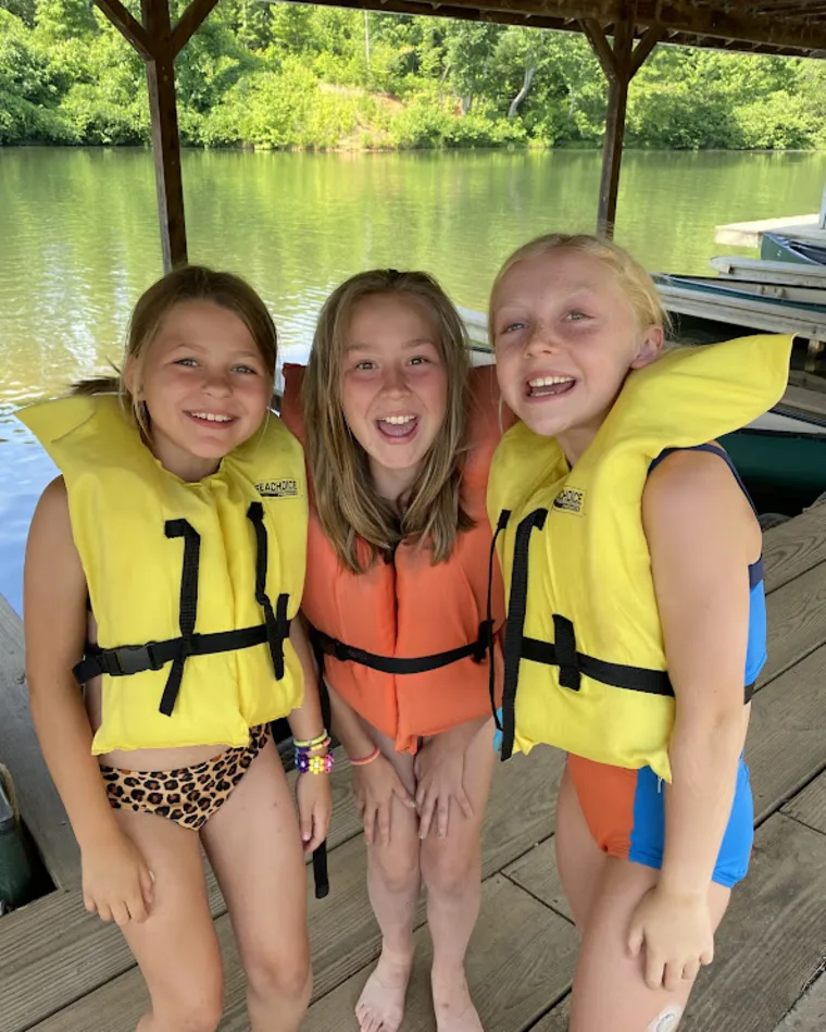 Three campers in life jackets laughing together on the dock