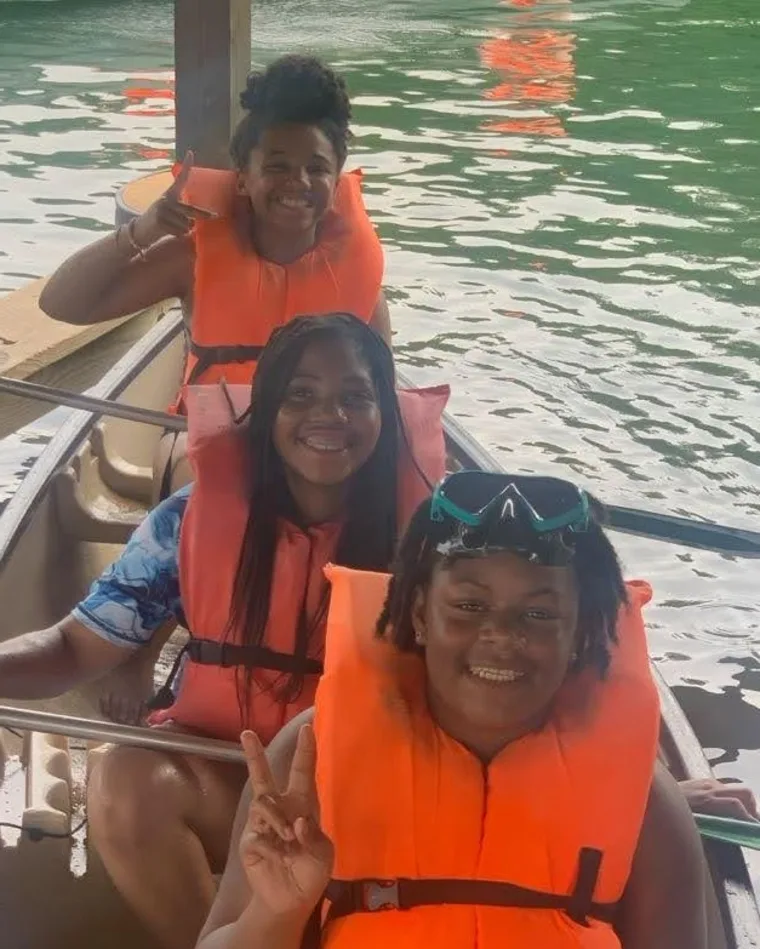 Three campers in life jackets making peace signs from a canoe