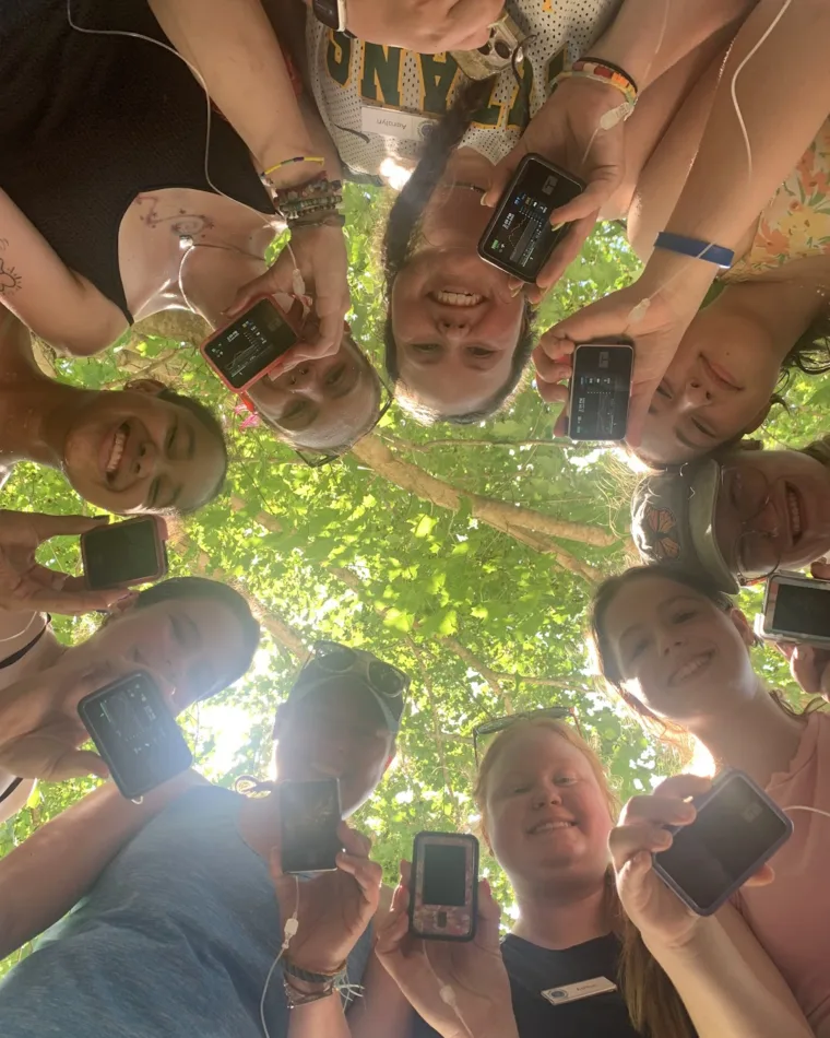 Campers and counselors in a circle under the trees, each holding up their glucose monitor