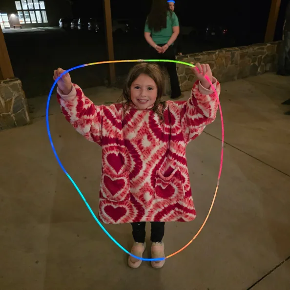 A young girl holding a glowing rainbow hoop above her head on the pavilion after dark