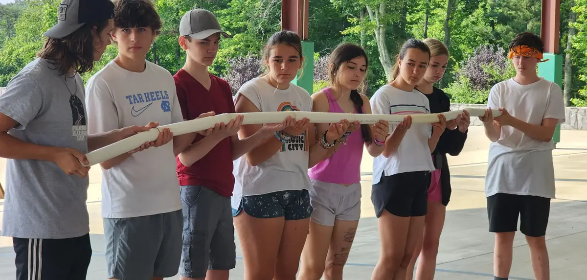A line of teens holding one long wooden beam together during a team challenge