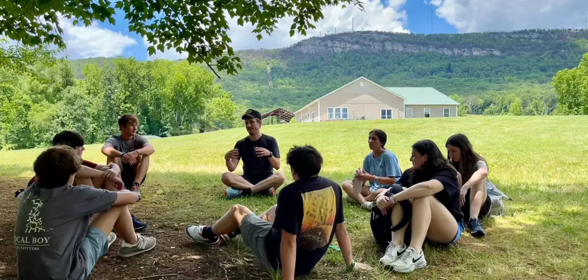 Teens sitting in a circle on the hillside with the ridge behind them