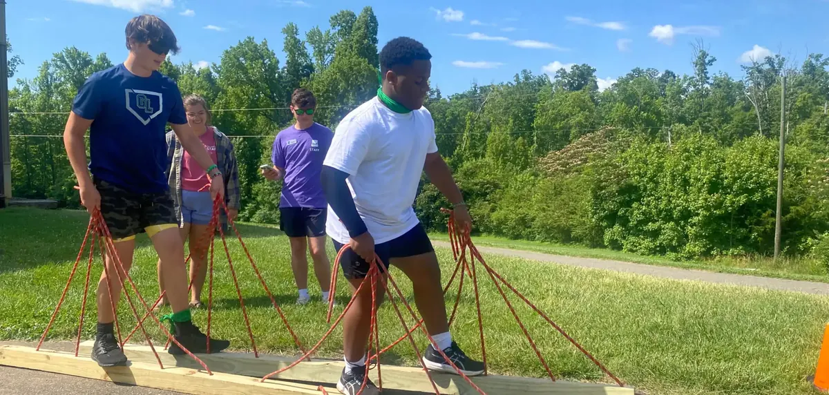 Teens crossing a low ropes balance element while the rest of their group spots them