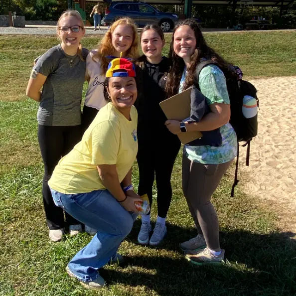Five people from the Teen Retreat crowded together for a photo on the grass, all grinning, one of them in a colourful propeller hat