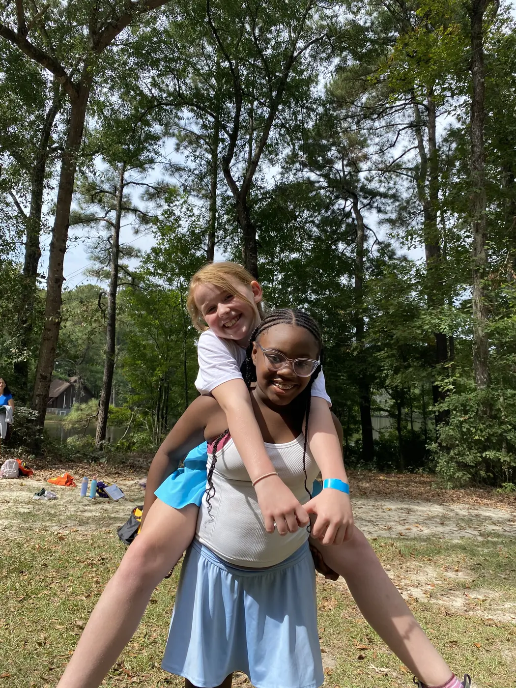Two campers laughing, one giving the other a piggyback ride by the lake at a Camp to Community day