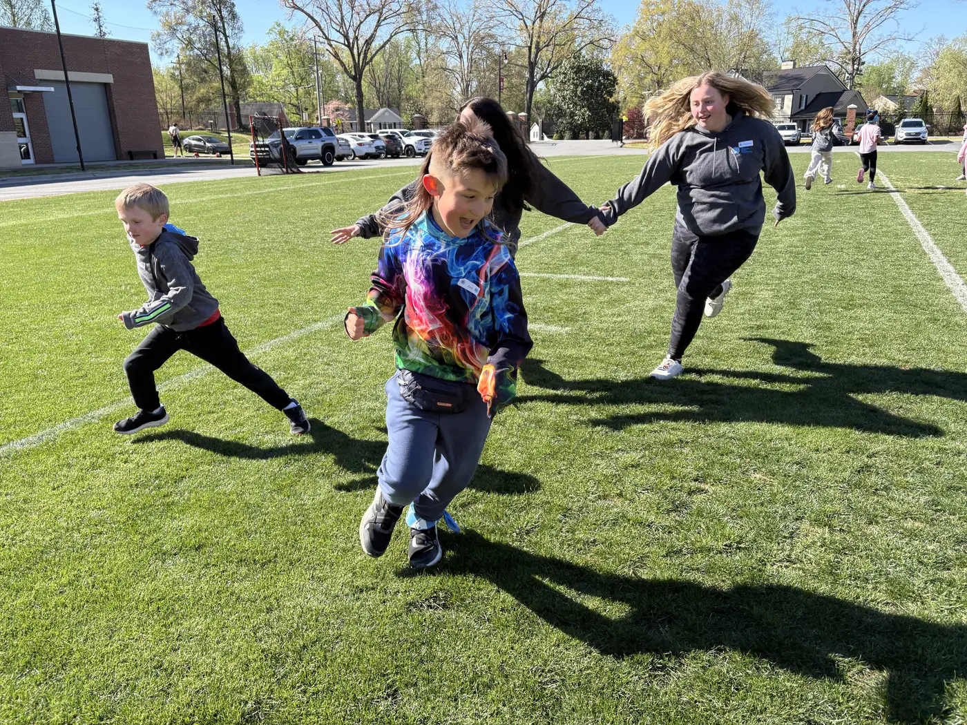 Children and a volunteer running across the field together during a Camp to Community game