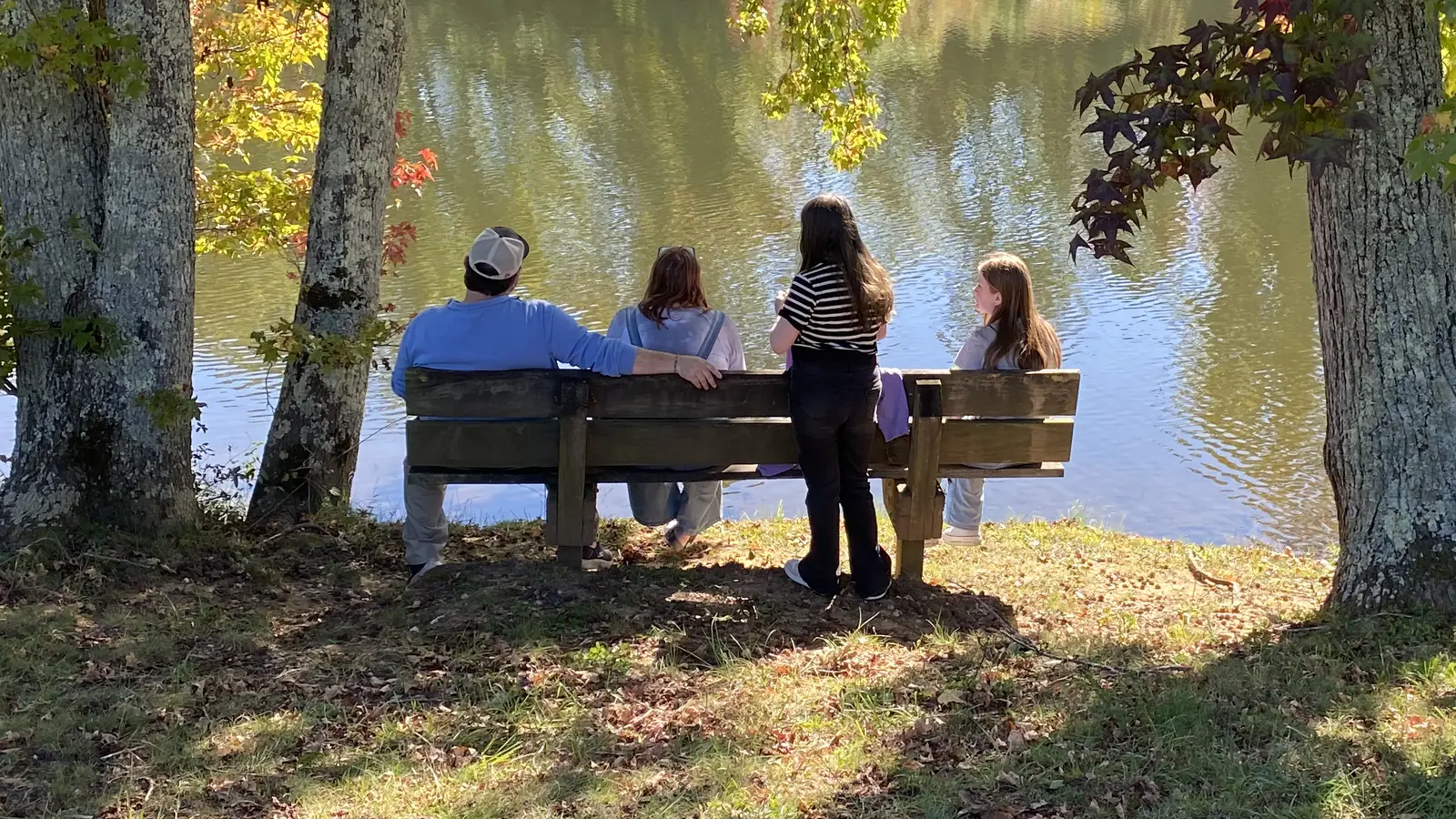 A family sits together on a bench beside the lake at the DFC Family Retreat, autumn trees around them