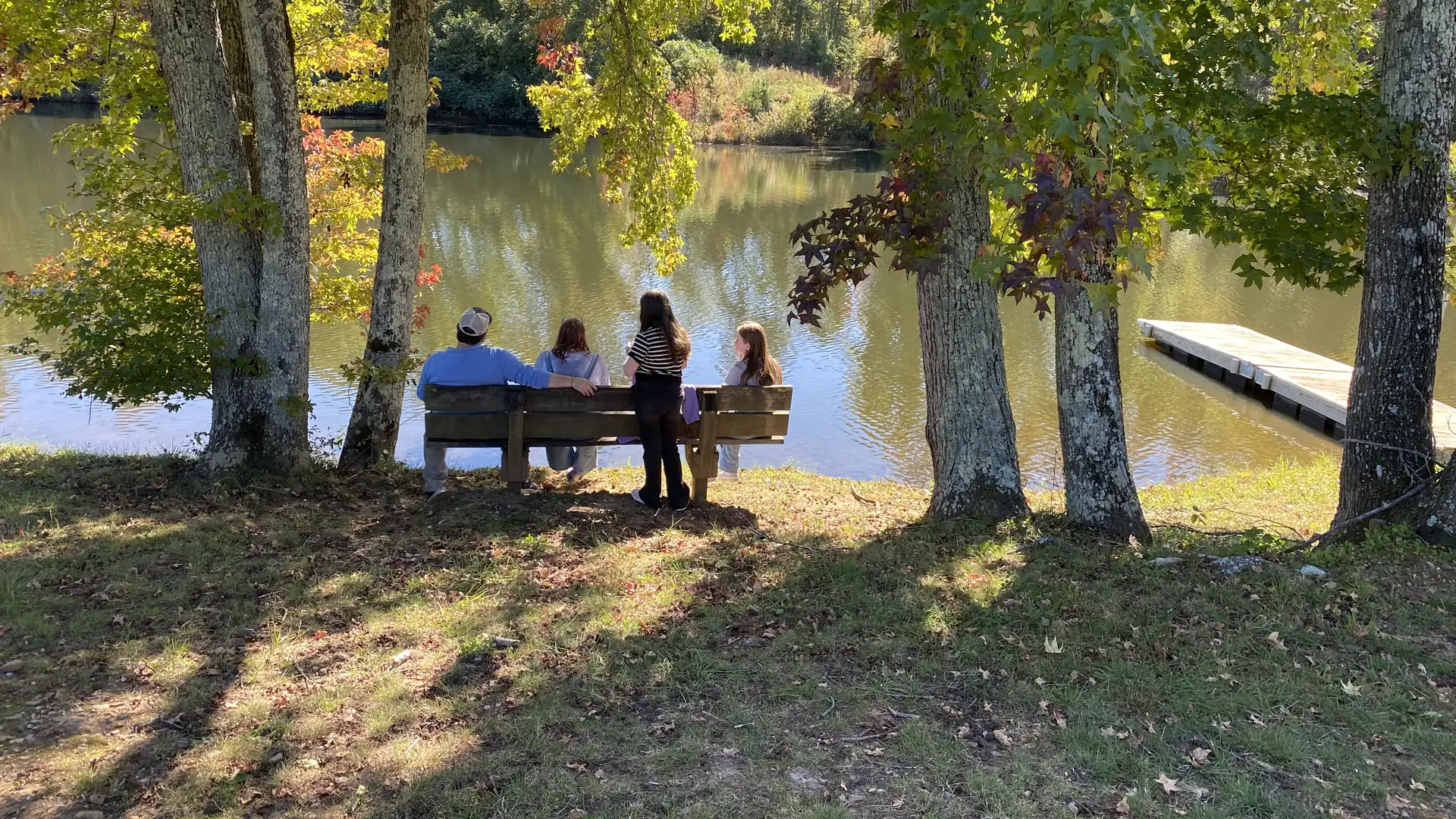 A family sits together on a bench under autumn trees, looking out over the lake at the DFC Family Retreat