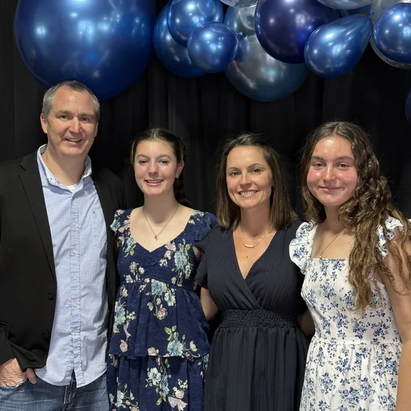 A family of four standing together in front of a cluster of blue and silver balloons at a Party with a Purpose fundraiser