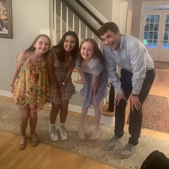 Three girls and a man leaning in together for a photo by the staircase at a Party with a Purpose held at home