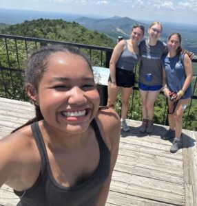Kennedy smiling in a selfie at a mountain overlook, three camp friends standing behind her at the railing