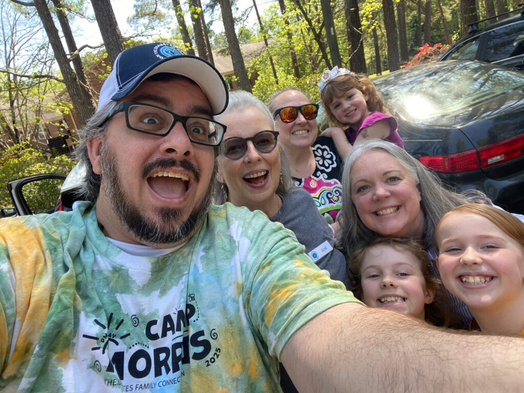 A group selfie of DFC volunteers and campers wearing Camp Morris shirts outdoors