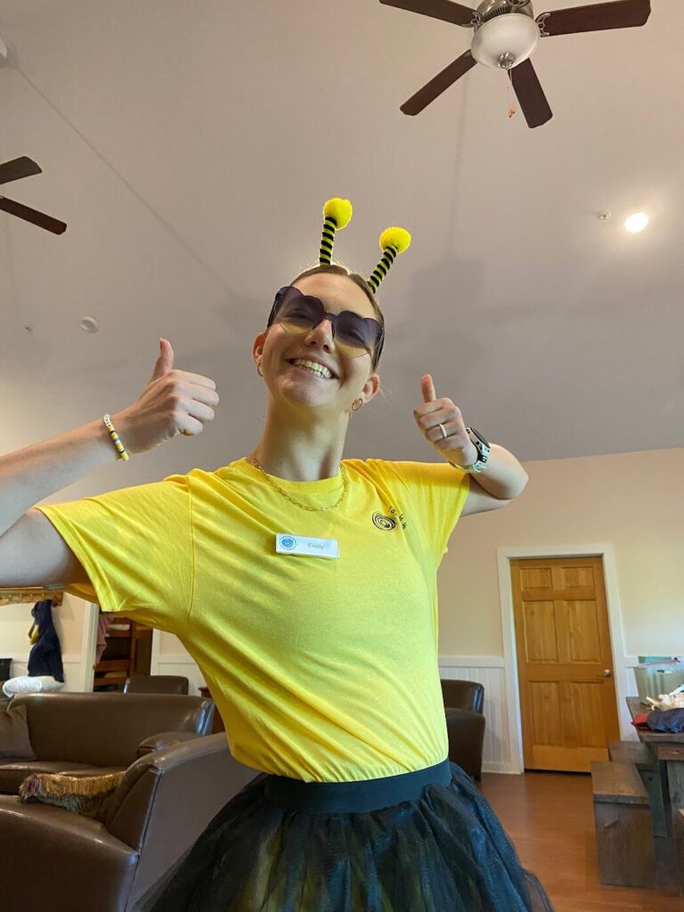 A DFC volunteer in a yellow shirt and bee antennae giving two thumbs up
