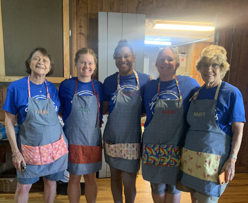 Five DFC volunteers wearing aprons while preparing a meal together