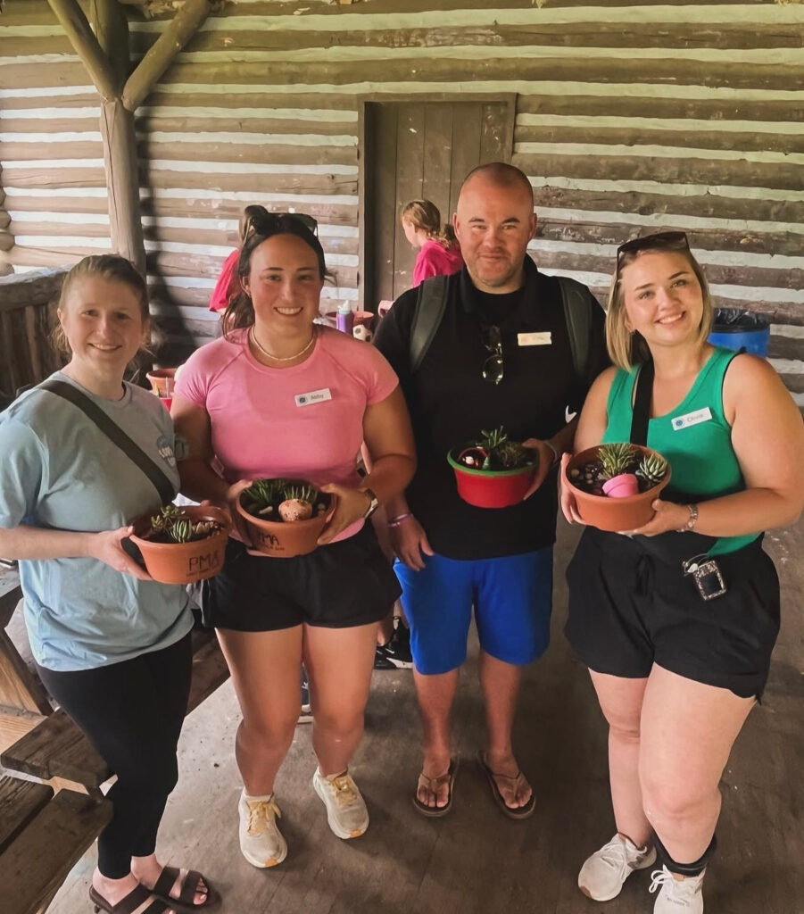 Four DFC volunteers holding potted plants outside a wooden cabin