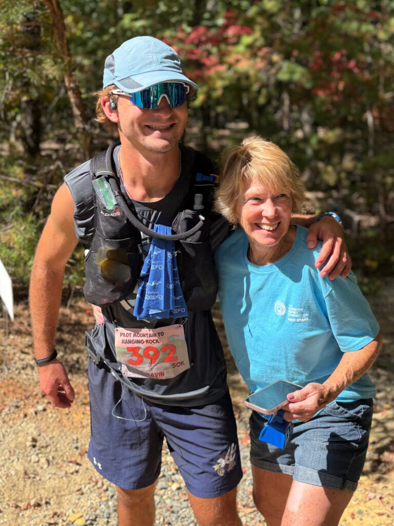 A runner wearing a race bib standing with a DFC volunteer on a wooded trail
