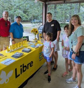 The Anthes family standing beside a sponsor table at a Camp to Community event