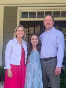 Caroline Gall standing between her mom and dad on the front porch of their home